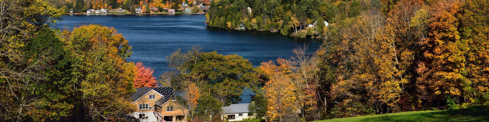 A lake surrounded by autumn-colored trees and houses on a hillside.
