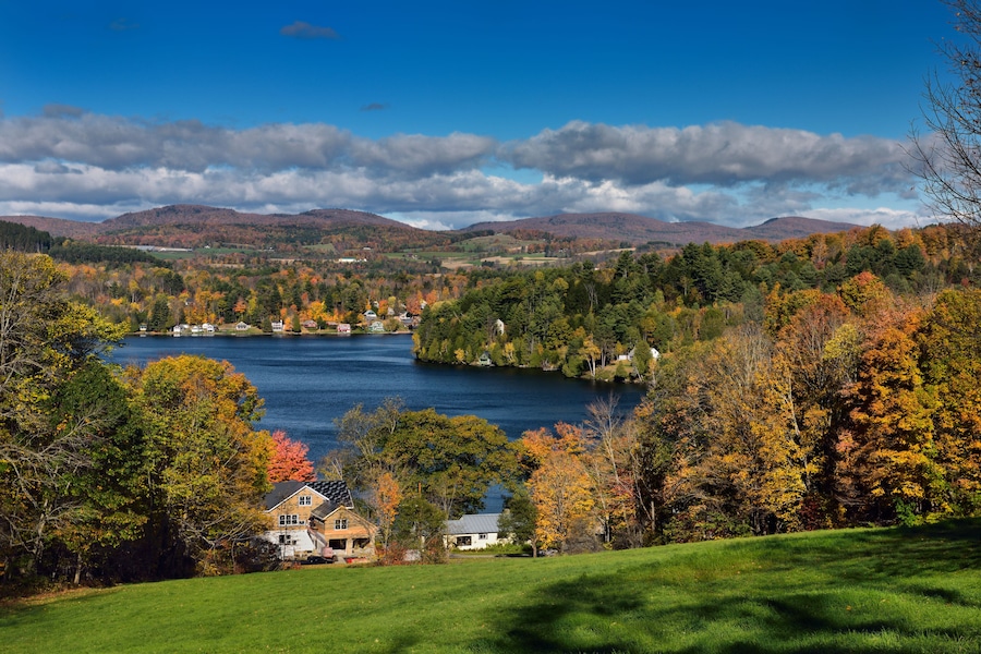 A lake surrounded by autumn-colored trees and houses on a hillside.