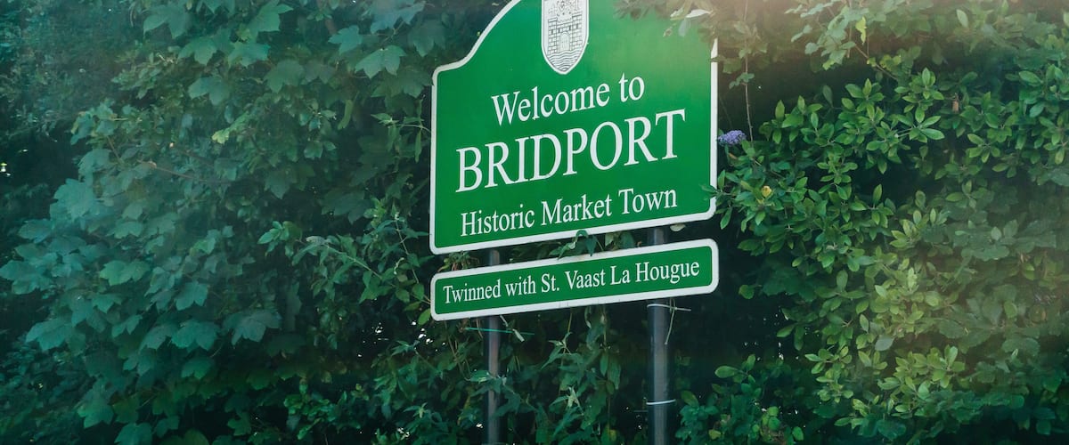 A green welcome sign for Bridport, Historic Market Town, twinned with St. Vaast La Hogue.