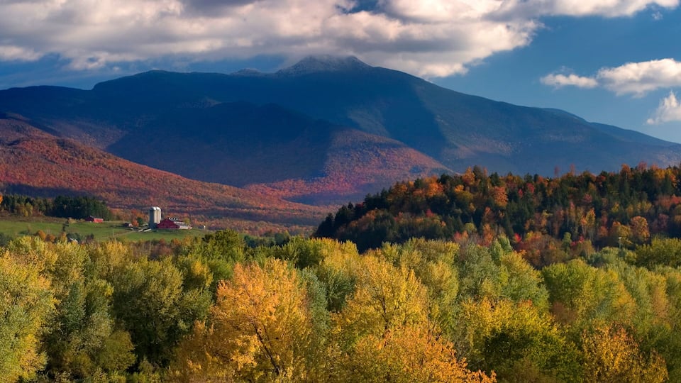 A mountainous landscape with autumn foliage, a red barn, and a silo.