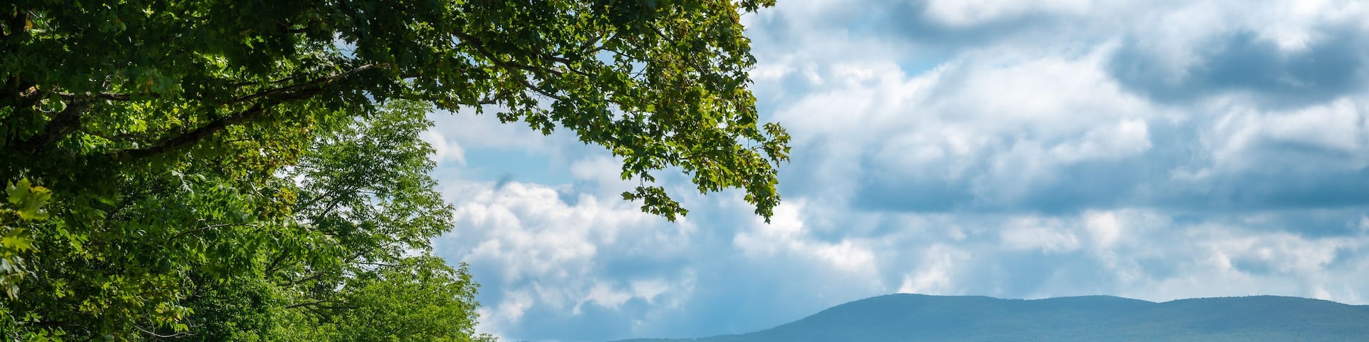 Rural landscape with dirt road, forest and mountain, Greensboro, Vermont, New England, United States. Photo taken in August 2023.