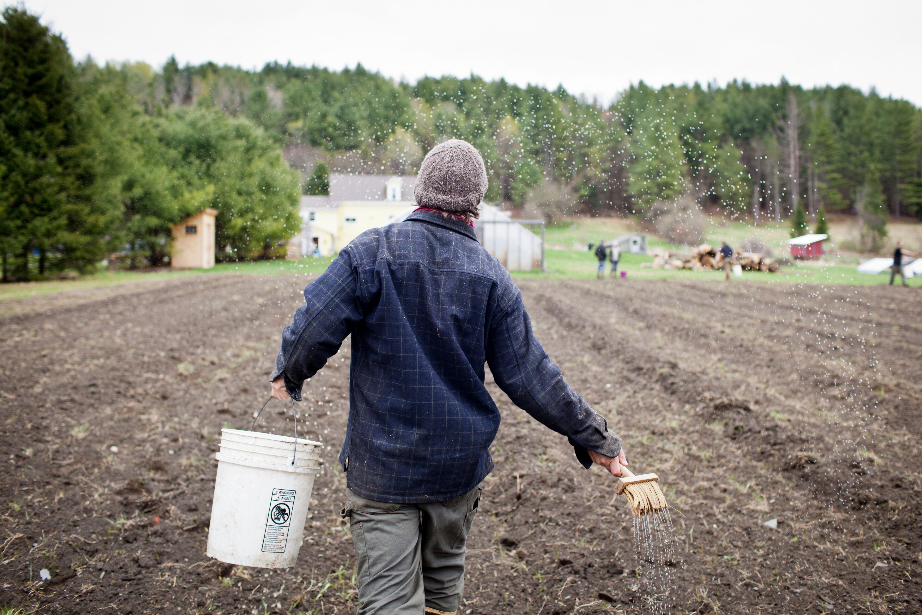 A person in a field holding a bucket and a watering can.