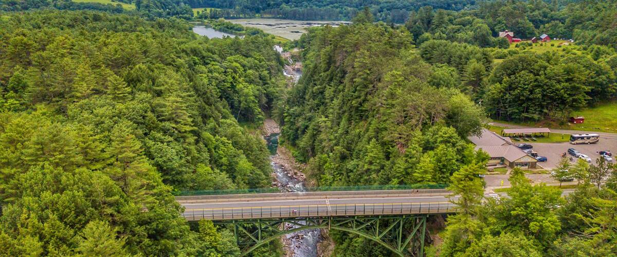 A bridge over a river surrounded by dense forest and hills.
