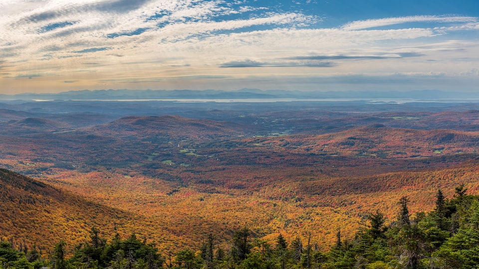 A mountainous landscape with autumn foliage and a distant view of a lake.