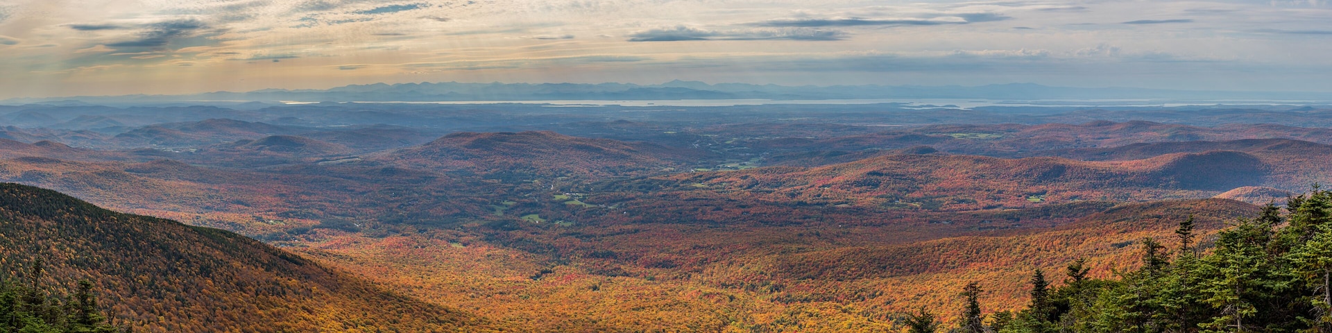 A mountainous landscape with autumn foliage and a distant view of a lake.