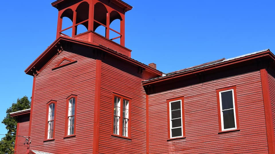 A red wooden building with a bell tower and multiple windows.