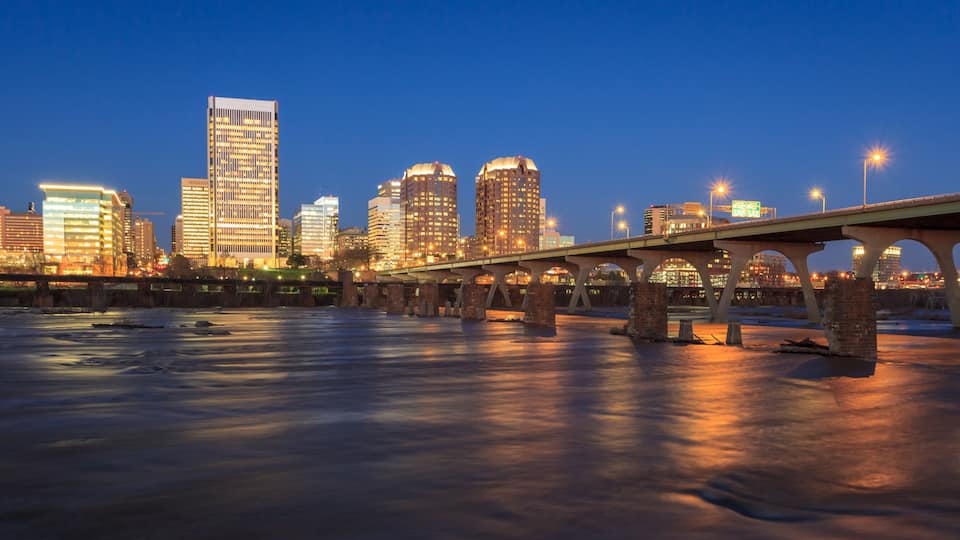 A city skyline at dusk with illuminated buildings and a bridge over a frozen river.