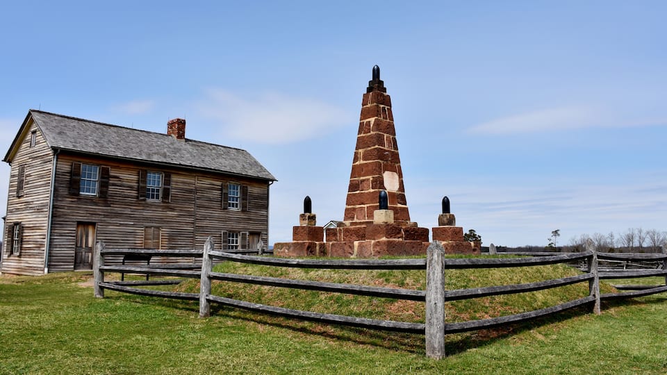 A wooden house and a stone monument with cannons.