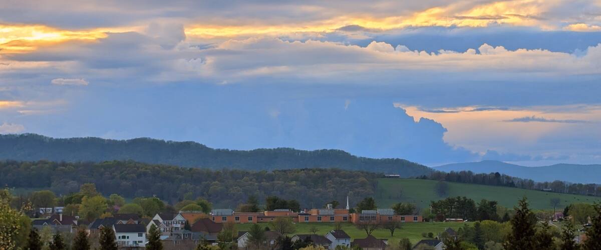 A rural landscape with rolling hills, a small village, and a sunset sky with clouds.