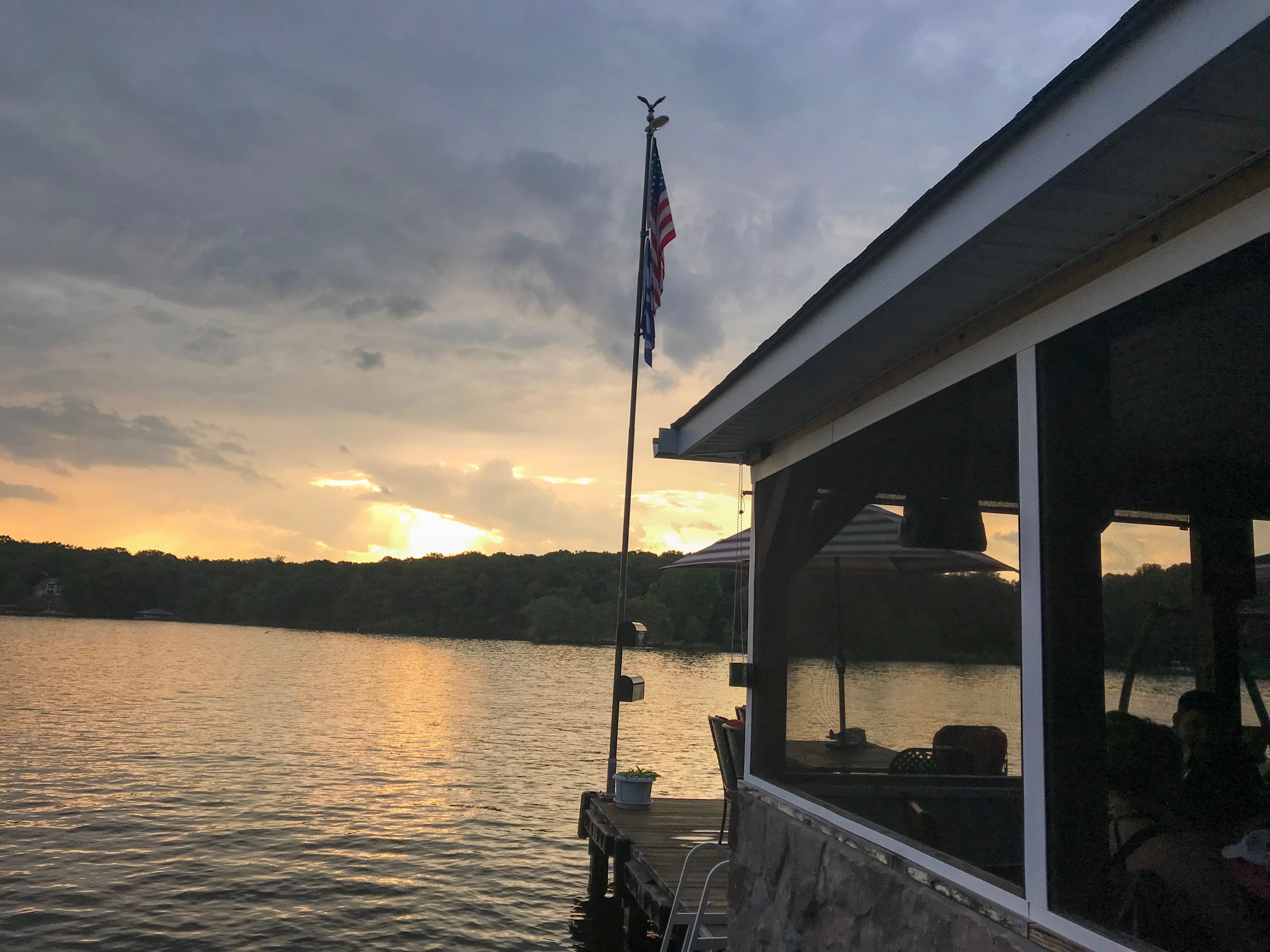 A lakeside view with a dock, a flagpole with an American flag, and a sunset in the background.