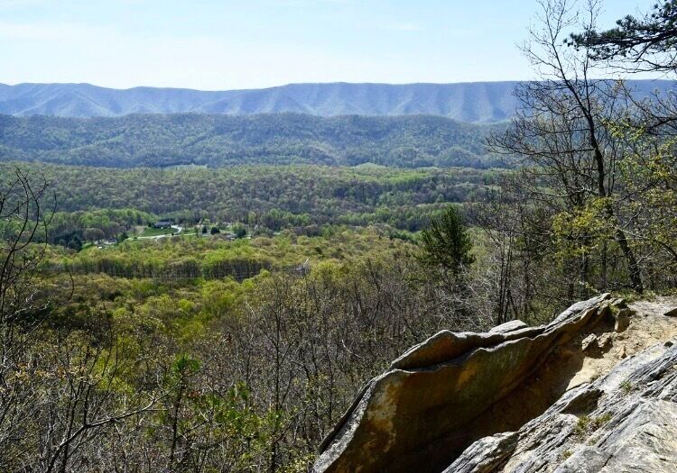 A mountainous landscape with a rocky outcrop in the foreground and a valley with trees in the background.
