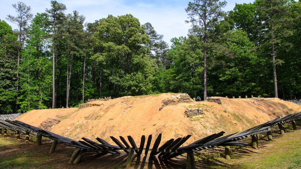 A dirt hill with a wooden fence in a forested area.