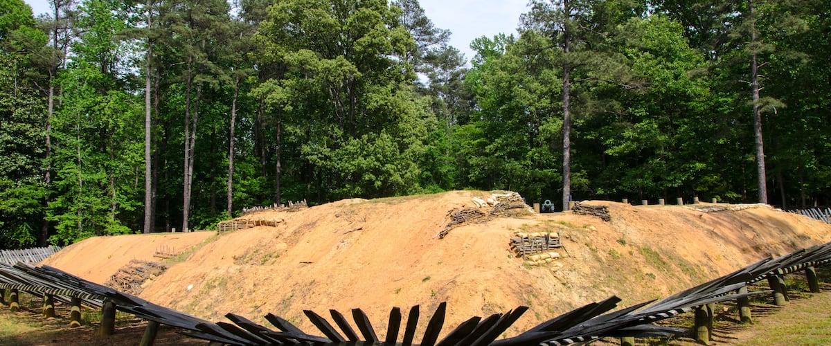 A dirt hill with a wooden fence in a forested area.