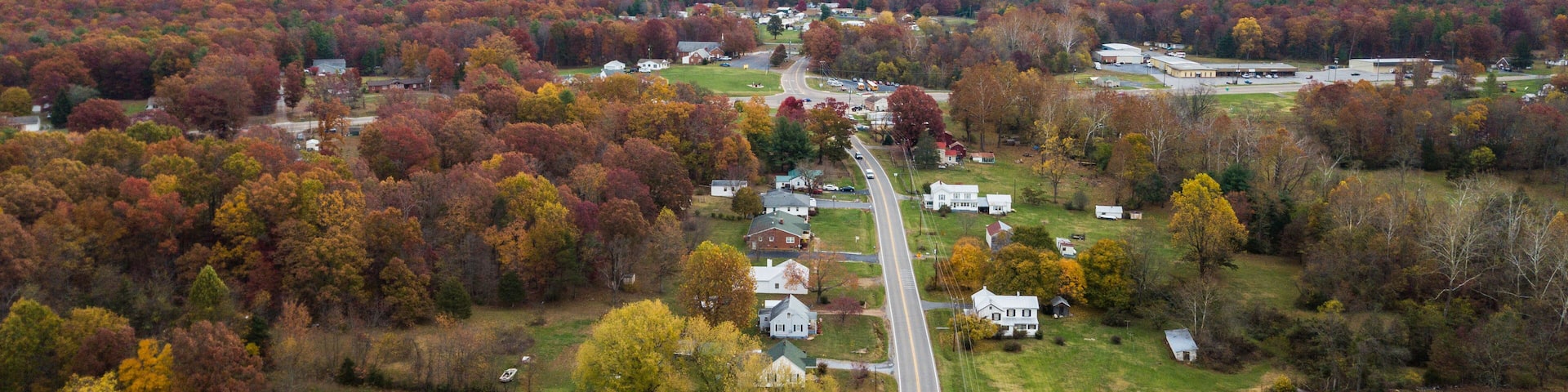A rural landscape with a winding road, houses, and autumn-colored trees.