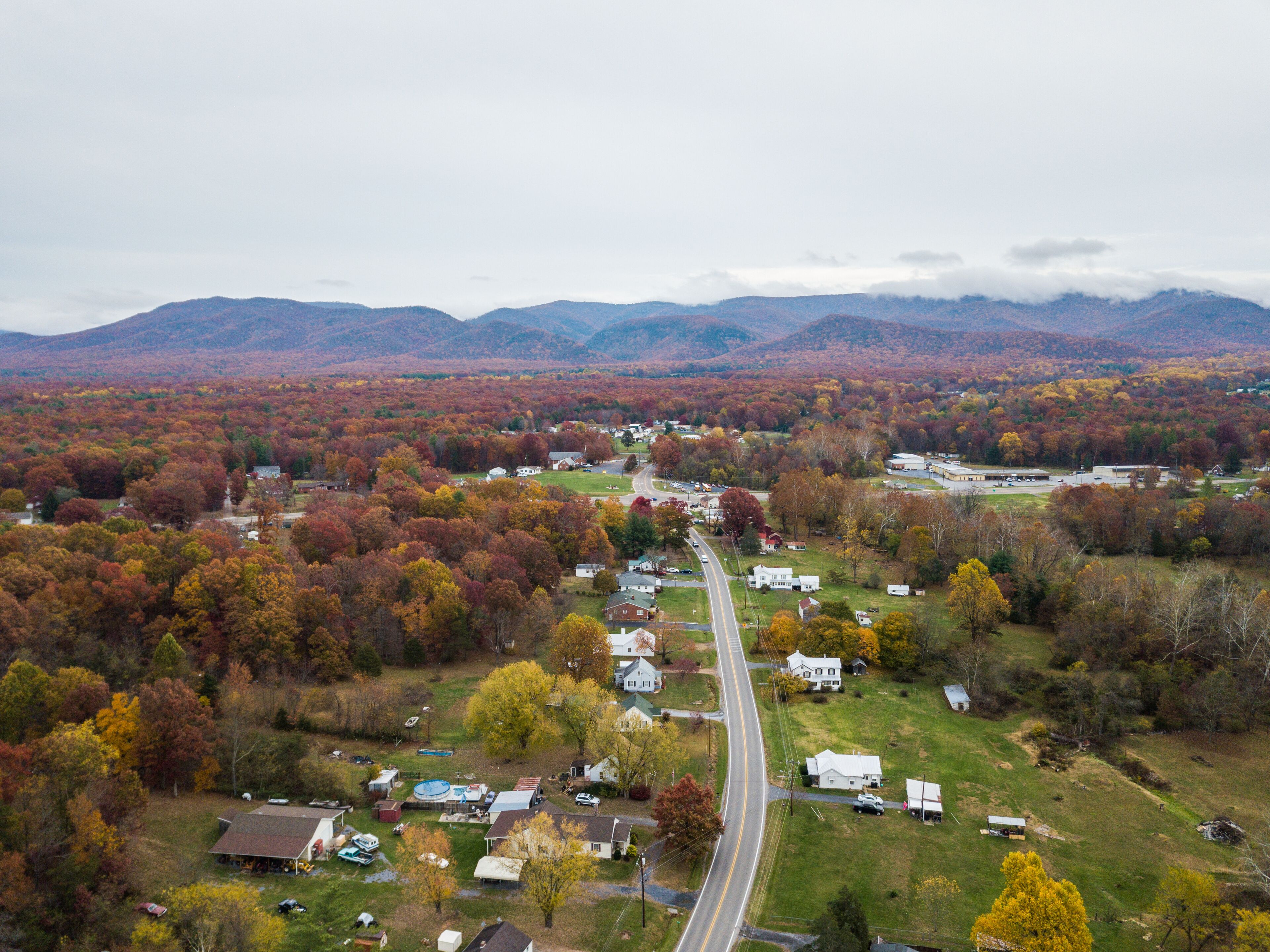 A rural landscape with a winding road, houses, and autumn-colored trees.