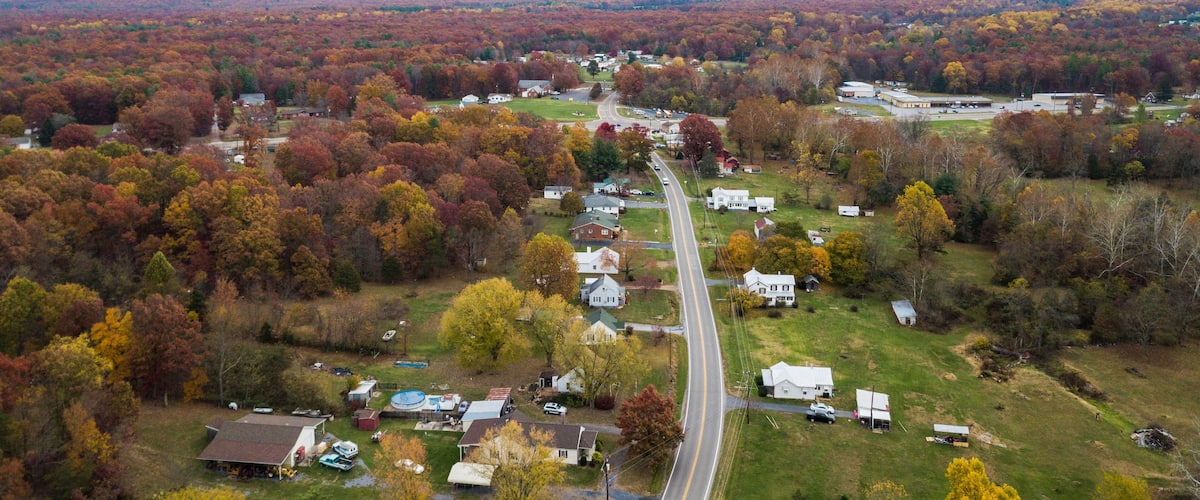 A rural landscape with a winding road, houses, and autumn-colored trees.
