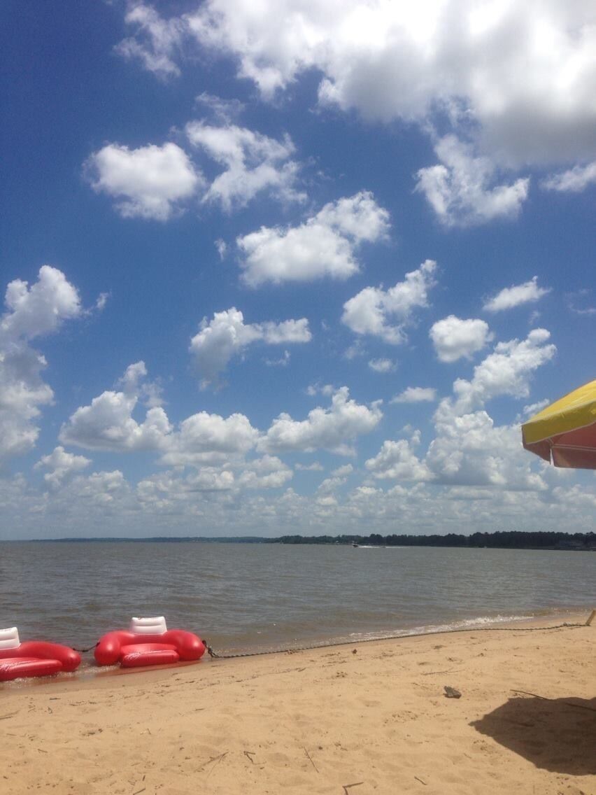 A beach with a clear sky, red beach balls, and a yellow umbrella.