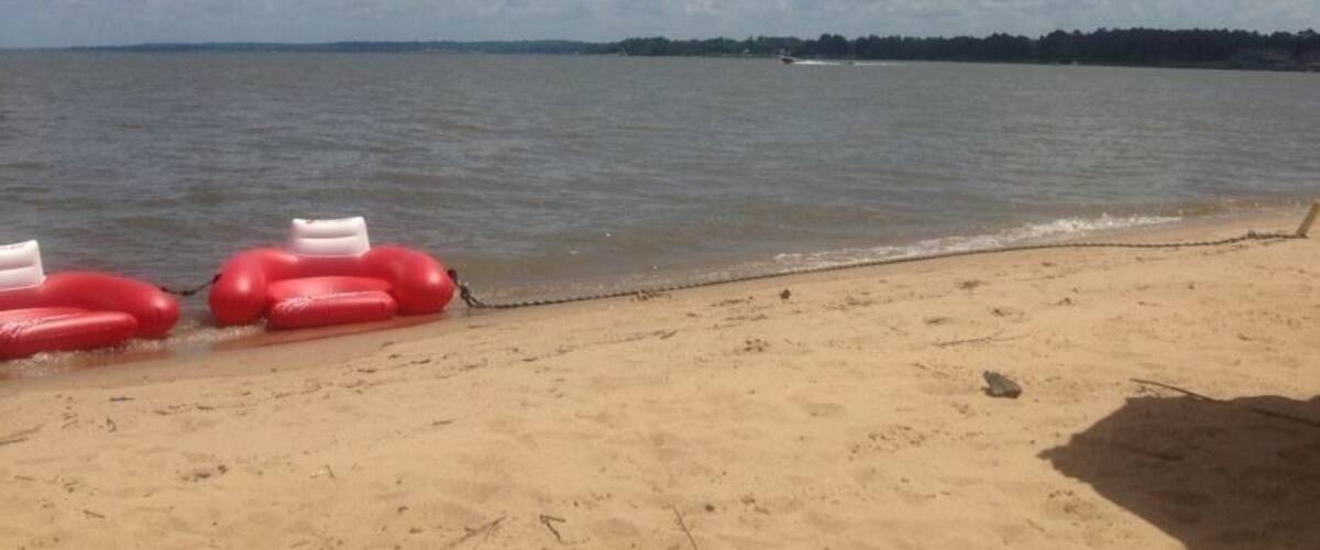 A beach with a clear sky, red beach balls, and a yellow umbrella.