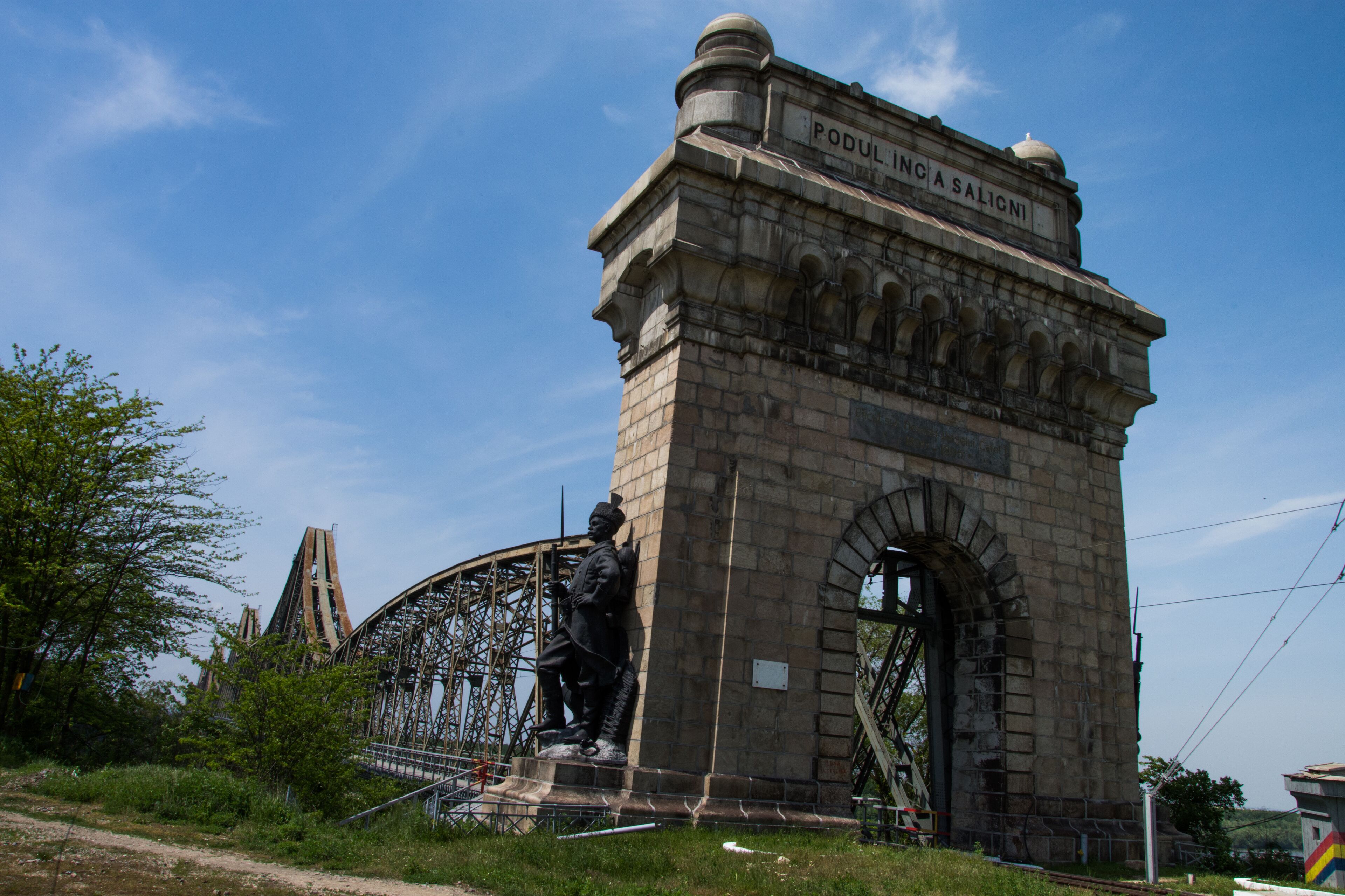 A stone monument with inscriptions, a statue, and a large metal structure in the background.