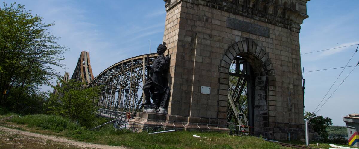 A stone monument with inscriptions, a statue, and a large metal structure in the background.