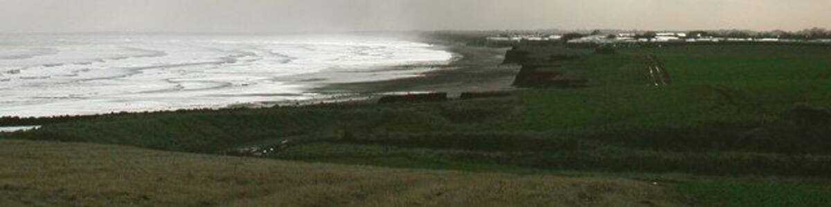 South Field, Barmston, East Riding of Yorkshire, England. Looking south across Barmston Drain towards Ullrome caravan park. There's an odd little bit of Barmston parish just south of here, where the parish boundary wanders out across the beach and back inland at 'Highlands' just north of the caravan park in the picture. Whatever feature caused the boundary to take this course has long ago been lost to coastal erosion.