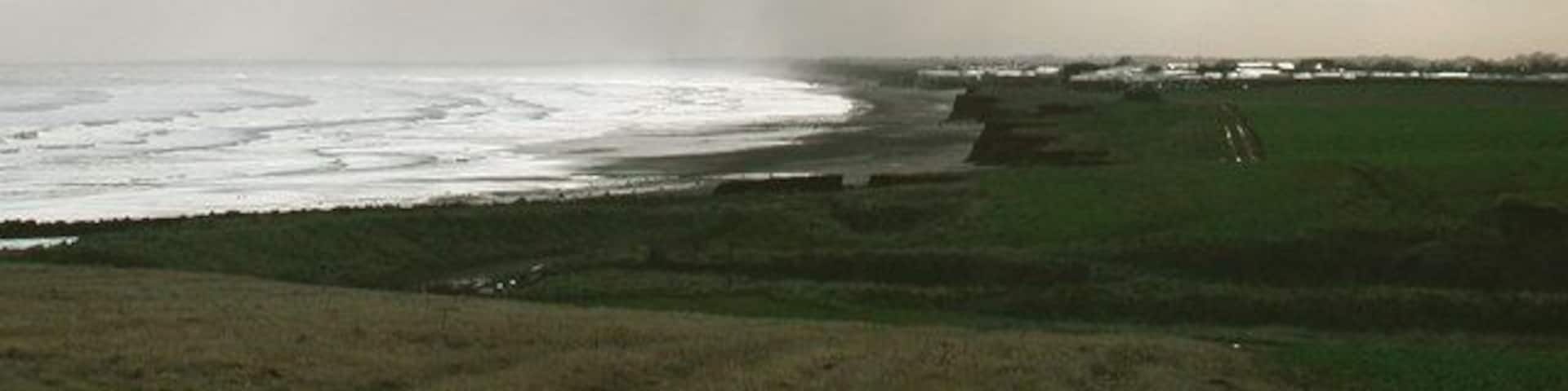 South Field, Barmston, East Riding of Yorkshire, England. Looking south across Barmston Drain towards Ullrome caravan park. There's an odd little bit of Barmston parish just south of here, where the parish boundary wanders out across the beach and back inland at 'Highlands' just north of the caravan park in the picture. Whatever feature caused the boundary to take this course has long ago been lost to coastal erosion.