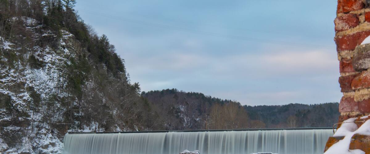 A snow-covered waterfall with a brick wall in the foreground.