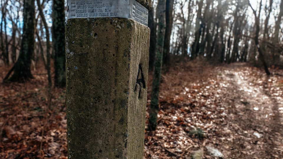 A wooden post with a sign indicating distances to various trails.