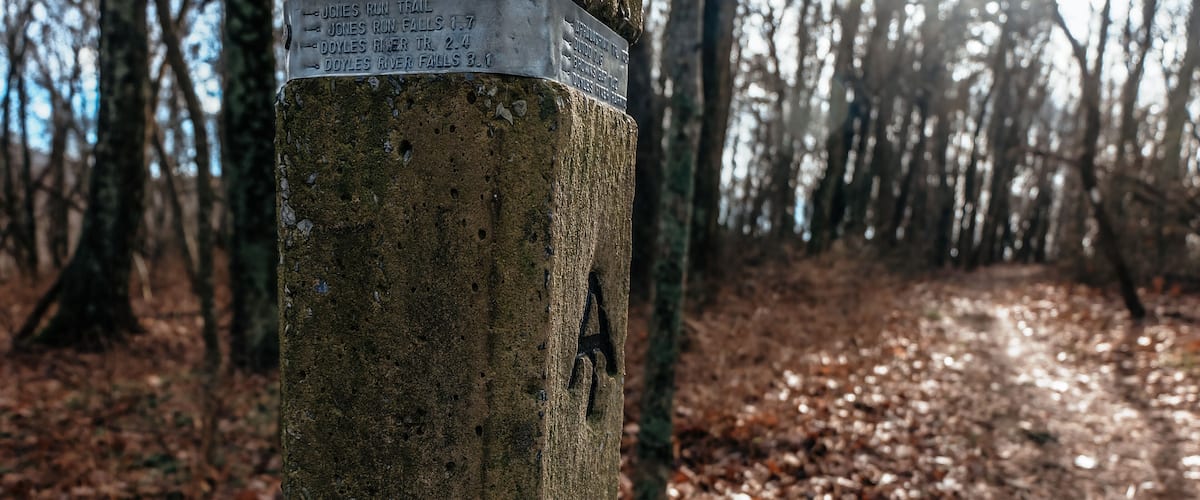 A wooden post with a sign indicating distances to various trails.