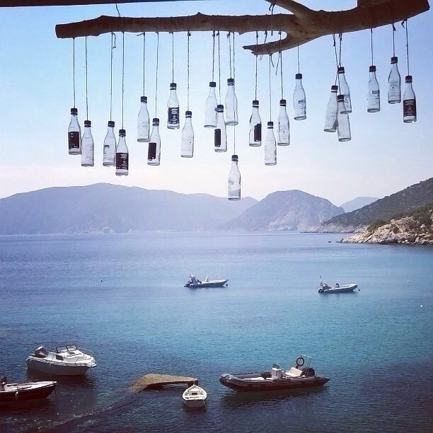 A lake with boats, a tree branch with hanging bottles, and mountains in the background.