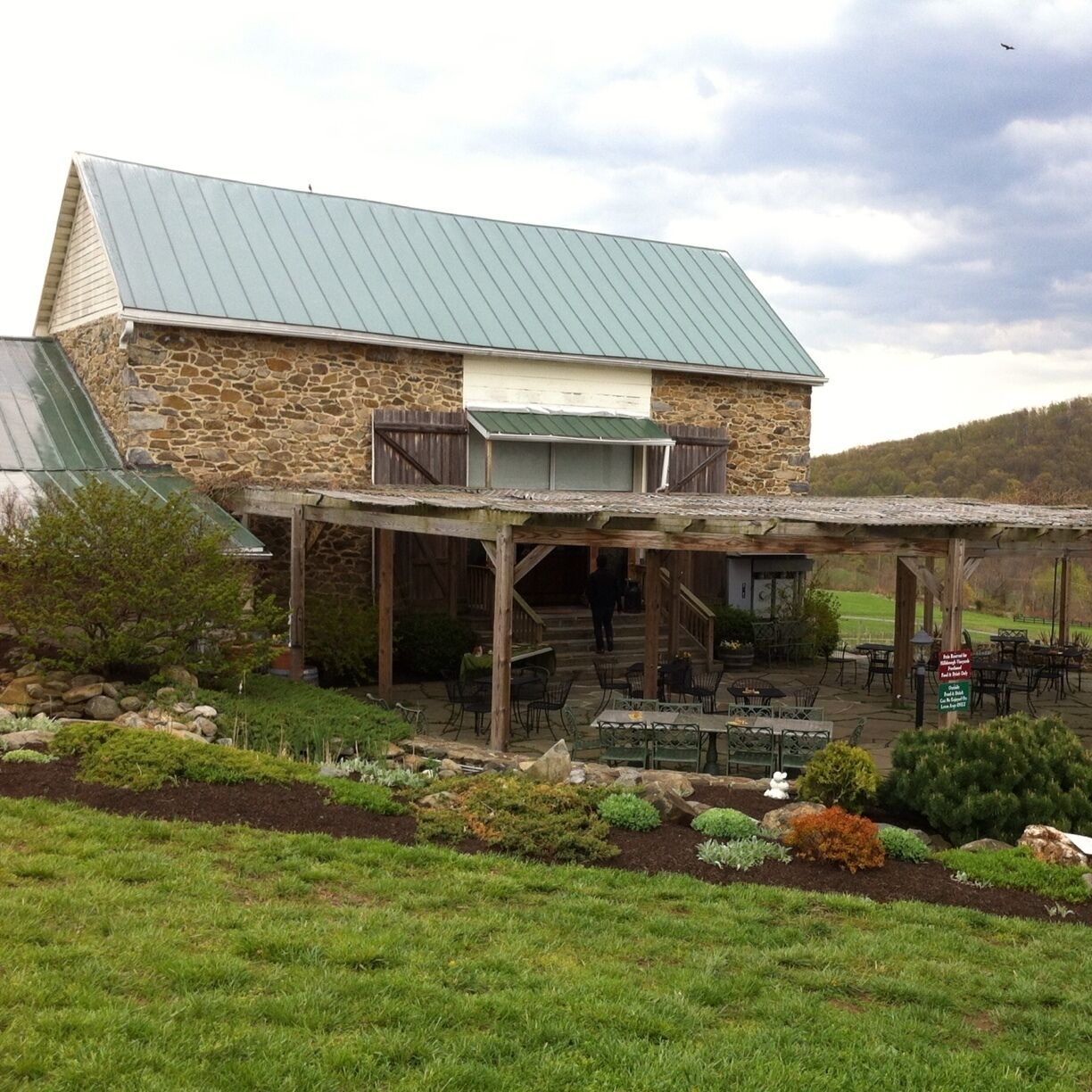 A stone building with a green roof and a covered patio area with outdoor seating.