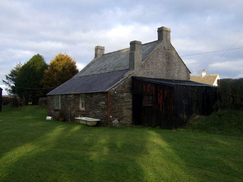A stone house with a sloped roof and a black barn.
