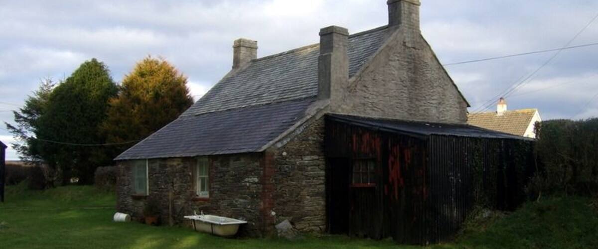 A stone house with a sloped roof and a black barn.