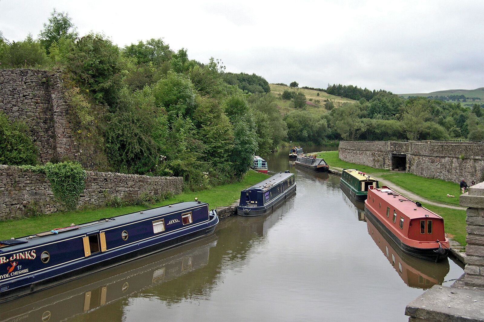 A narrow canal with boats, stone walls, and greenery.