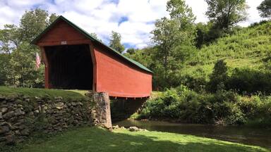 A red covered bridge with the number 1916, a stone wall, a grassy area, and a river.