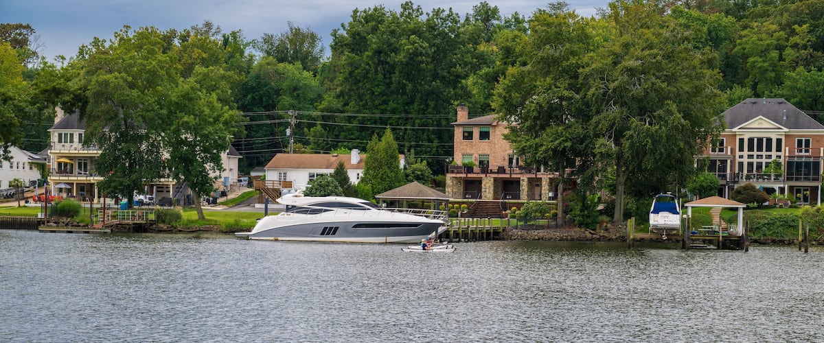 A white yacht docked at a marina with houses and trees in the background.