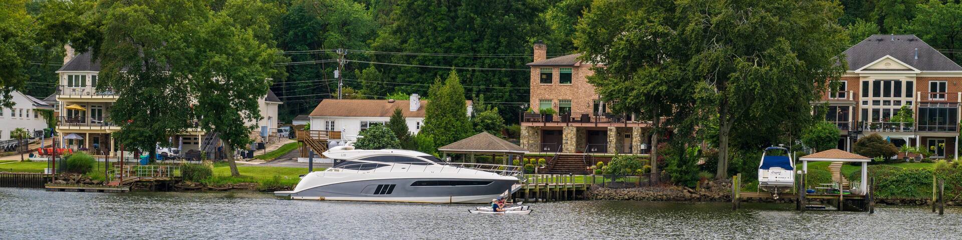 A white yacht docked at a marina with houses and trees in the background.