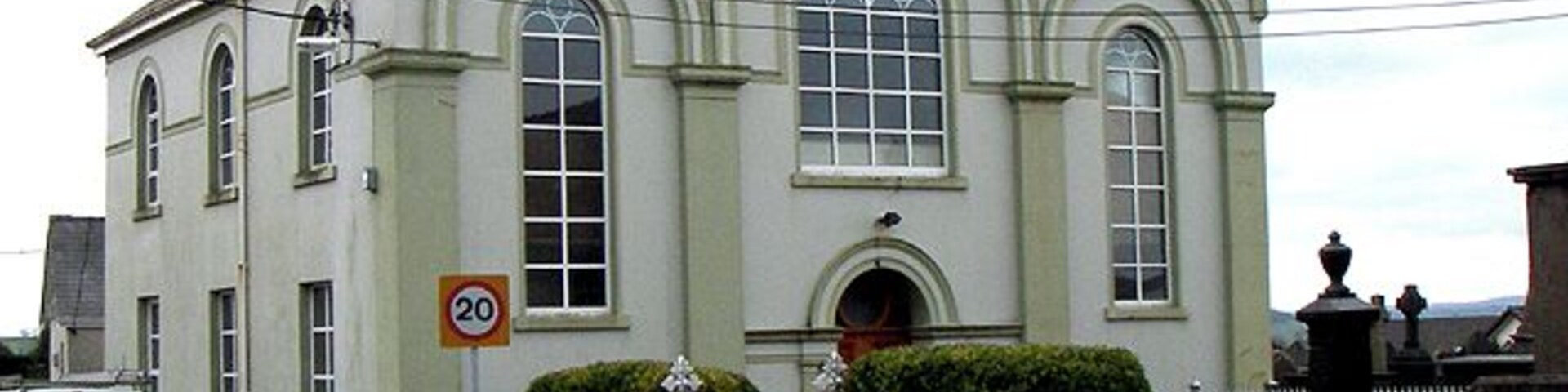 A white church with a 20 mph speed limit sign, a white fence, and a statue in front.