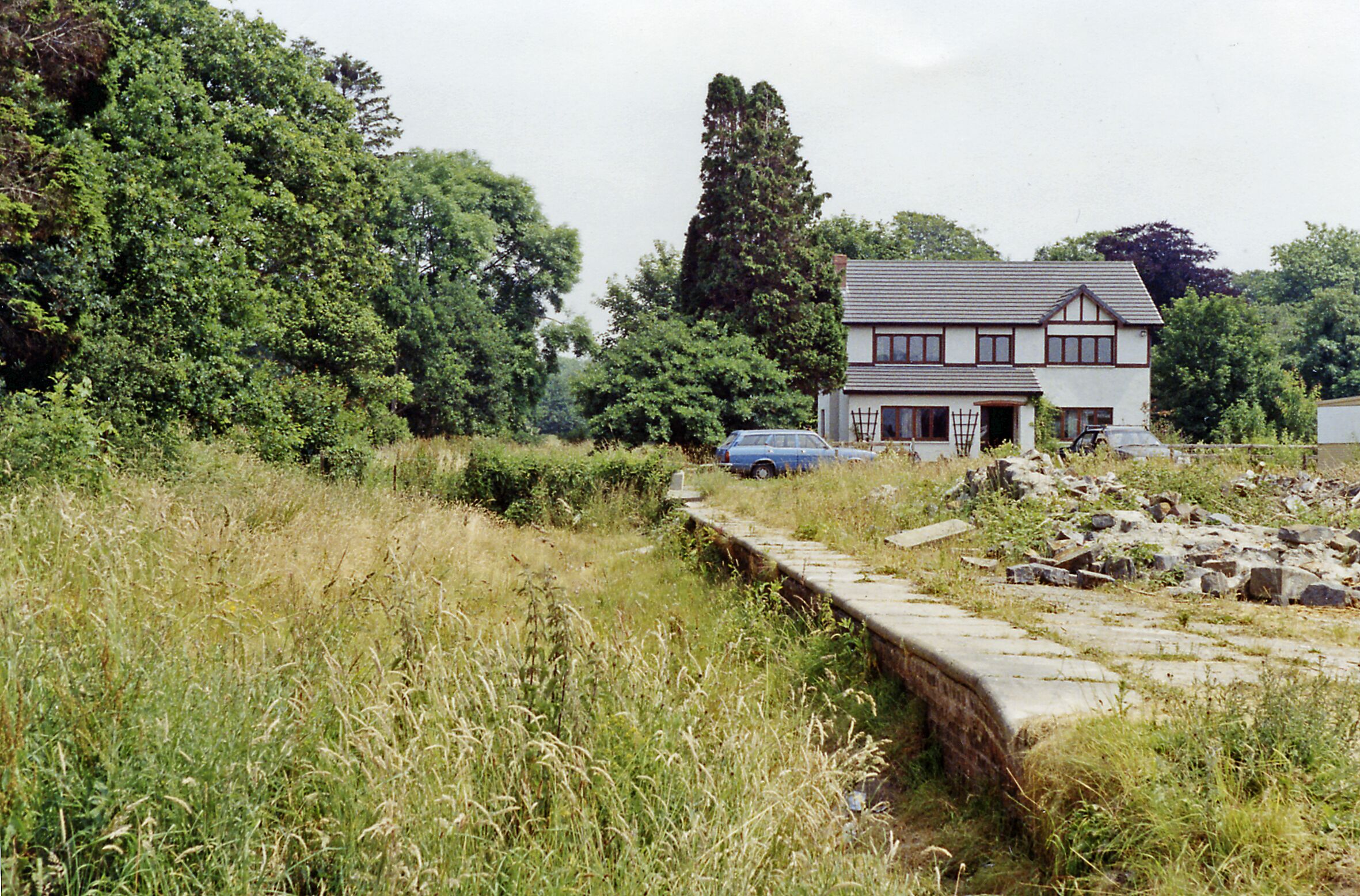 A house surrounded by dense greenery and a stone wall.