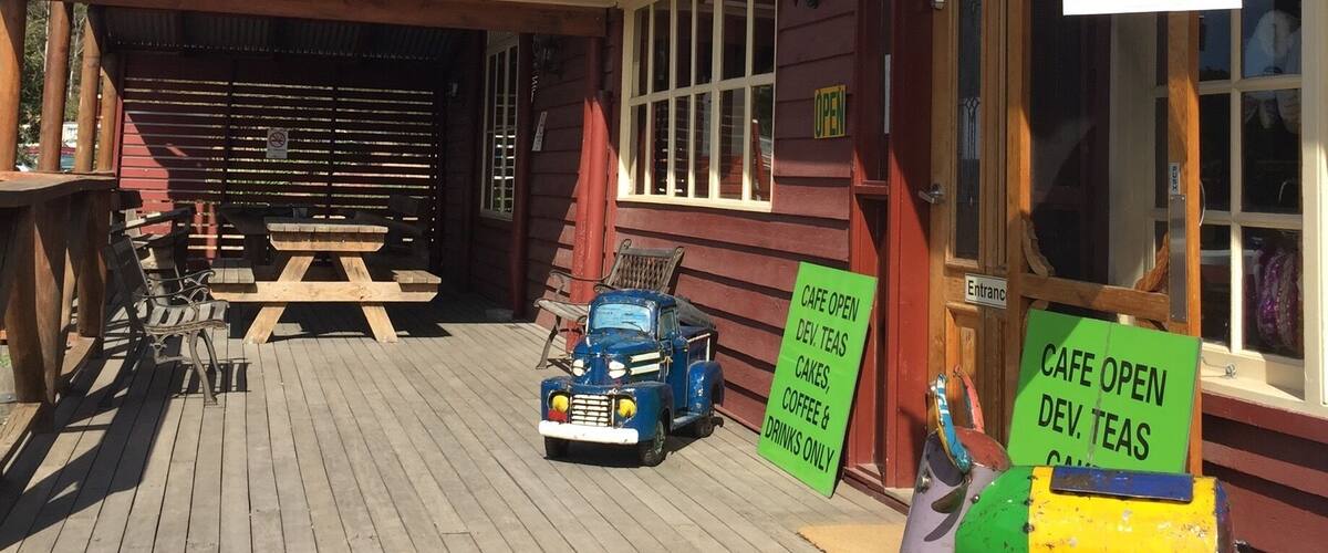A rustic cafe with a wooden deck, vintage cars, and a sign advertising Fanta.