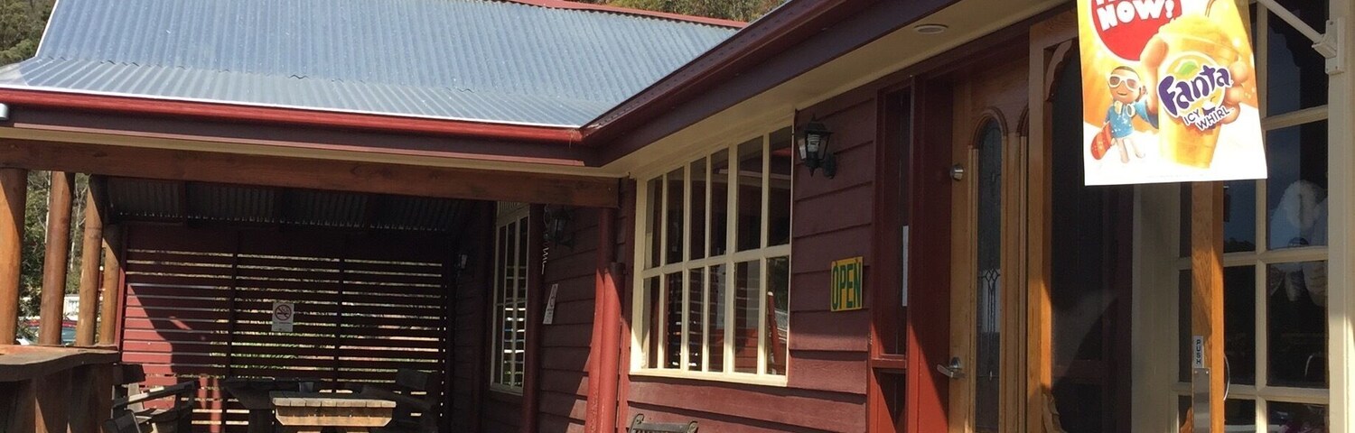 A rustic cafe with a wooden deck, vintage cars, and a sign advertising Fanta.