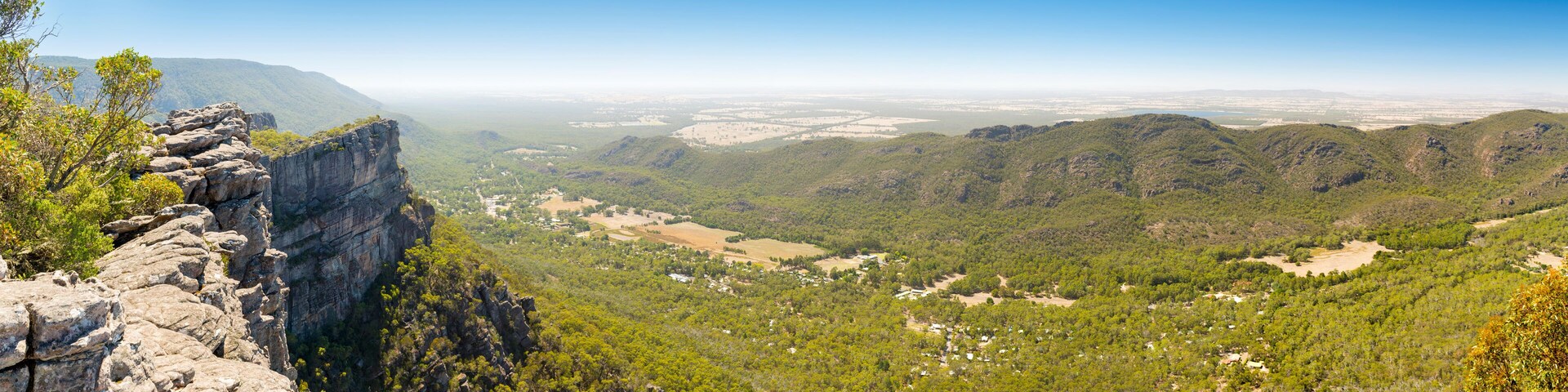 Paisagem montanhosa com uma formação rochosa em destaque à esquerda e um vale com edifícios dispersos.