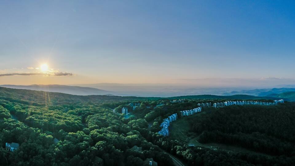 Aerial view of a sun-kissed mountain ridge covered in lush green trees, with a distant row of houses nestled among the foliage, Rileyville, Virginia, USA.