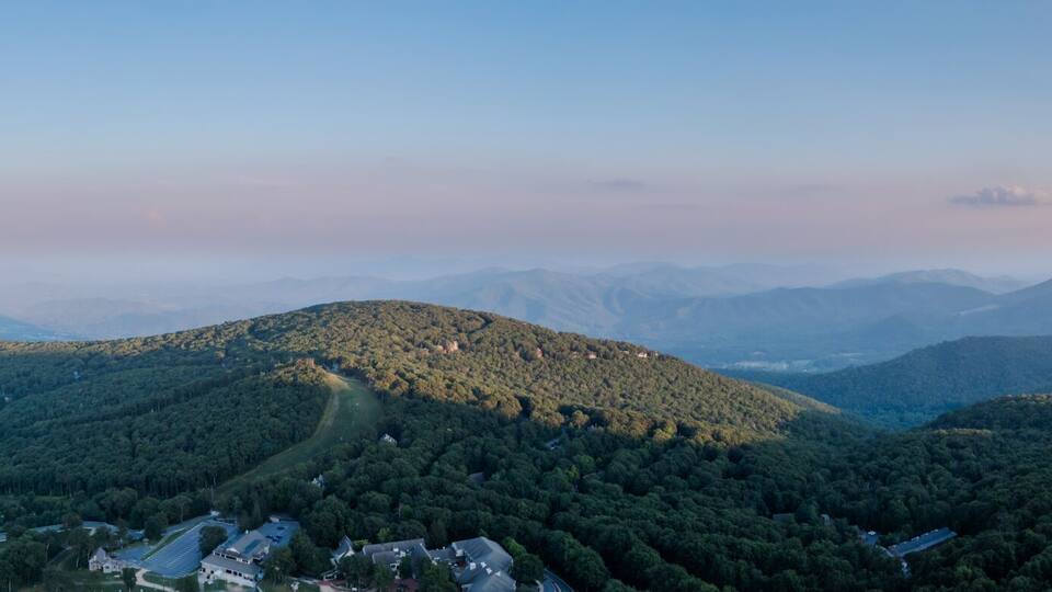 Aerial view of the sun rising over the lush, green, forested mountains, casting long shadows and illuminating a tower on the peak, Rileyville, Virginia, USA.