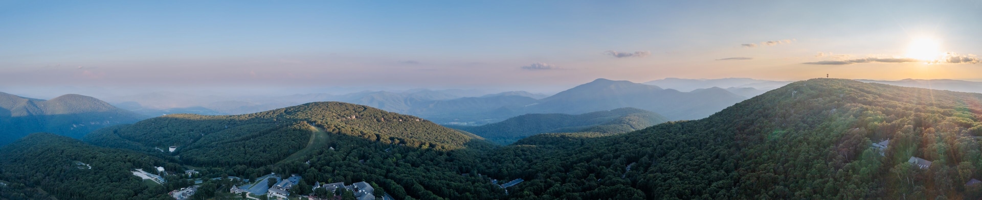 Aerial view of the sun rising over the lush, green, forested mountains, casting long shadows and illuminating a tower on the peak, Rileyville, Virginia, USA.