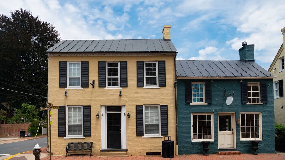 A two-story building with black shutters, a bench, and a street corner.