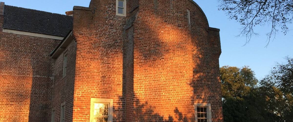 A brick building with a prominent chimney and two windows.