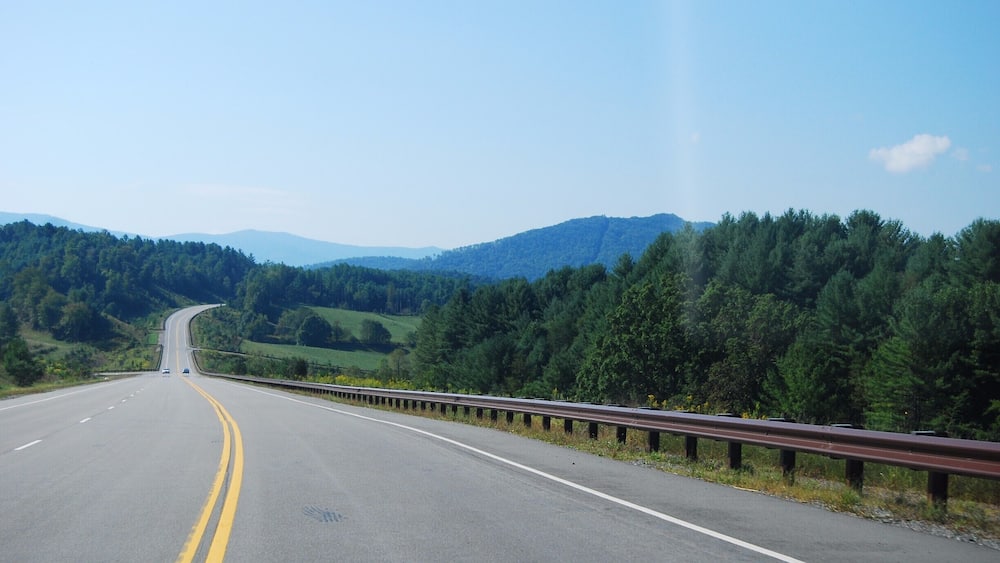 A highway curving through a mountainous landscape with dense forests on both sides.