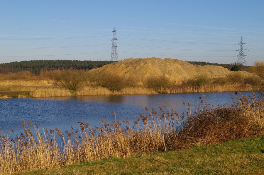 Fishing lake and sand pile The fishing lake is part of the Nar Valley Fisheries. The lakes are former sand pits, as is suggested by the pile of sand behind this one.