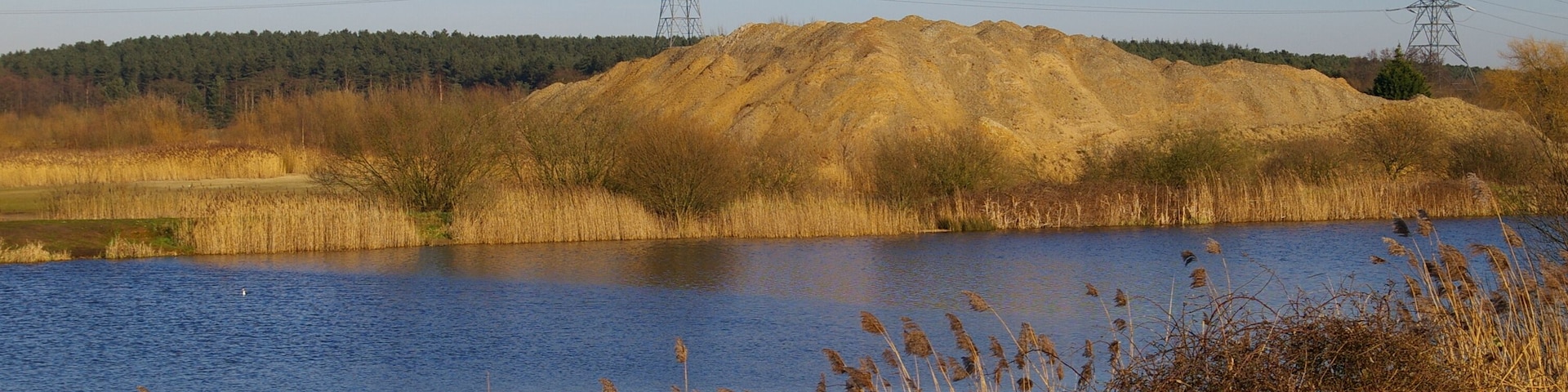 Fishing lake and sand pile The fishing lake is part of the Nar Valley Fisheries. The lakes are former sand pits, as is suggested by the pile of sand behind this one.
